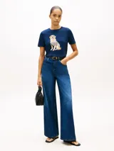 Remera de manga corta azul marino con cuello redondo, confeccionada en algodón. Presenta un diseño gráfico bordado en el pecho de un perro Golden Retriever vestido con una camiseta a rayas.