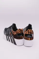 Zapatillas urbanas negras con plataforma blanca y detalles a rayas en el talón y la suela. Presentan un diseño con múltiples tiras elásticas en el empeine y puntera charolada.