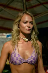 Conjunto de bikini color crema con estampado de monogramas en color lila. El corpiño es triangular con tiras para atar y la bombacha es vedetina con reguladores metálicos.