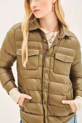 Campera puffer de corte camisero en color verde militar, con cierre frontal mediante botones a presión, bolsillos superiores con solapa y puños tejidos en color beige.
