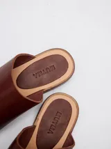 Sandalias planas de cuero color marrón, con diseño minimalista que sujeta el dedo pulgar y deja el empeine al descubierto.