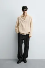 Camisa de manga larga color beige claro con textura jacquard arrugada, cuello solapa con abertura en V y bolsillo canguro frontal. Posee cordones ajustables en el bajo lateral.