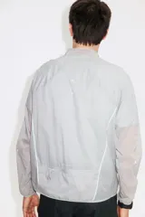 Campera deportiva liviana color gris, resistente al agua, con cuello elevado y cierre frontal. Cuenta con tecnología DryMove para absorber el sudor, mangas largas con puños elásticos y diseño plegable.