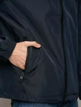 Campera ligera Calvin Klein de corte regular, confeccionada en tejido técnico resistente al viento. Presenta capucha con cordones ajustables, cierre frontal con cremallera, bolsillos laterales con cierre y puños elásticos.