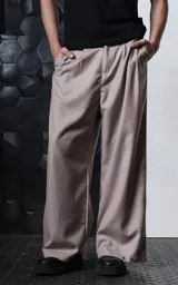 Pantalón sastrero de corte oversize en color beige, con pinzas frontales profundas que aportan volumen y movimiento. Presenta cintura ancha, bolsillos laterales y bolsillos tipo ojal en la parte trasera, con detalle de botones en el ruedo.
