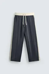 Pantalón jogger de corte wide fit en tejido compacto color gris oscuro. Presenta cintura elástica con cordón ajustable, bandas laterales en contraste color beige y costuras frontales tipo pinza.