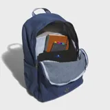Mochila Adidas de estilo clásico confeccionada en tejido de sarga de algodón color azul denim. Cuenta con un compartimento principal amplio, bolsillo frontal con cierre, bolsillos laterales elásticos y correas ajustables acolchadas con detalle de rayas. Presenta el logotipo del trébol de la marca en la parte inferior frontal.