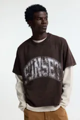 Remera de algodón color marrón con efecto lavado, cuello redondo y estampado frontal con la palabra 'SUNSET' en estilo universitario desgastado.