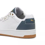 Championes Puma Court Classic de diseño urbano, color blanco con detalles en negro en la lengüeta y el talón. Presenta logo Puma en dorado en el lateral y la lengüeta, ojales superiores metálicos dorados y suela de goma color caramelo.