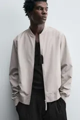 Cazadora bomber ligera de tejido técnico color verde oliva, con cuello, puños y bajo en rib elástico. Presenta cierre frontal de cremallera y bolsillos de vivo en la cadera.