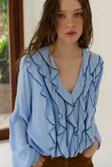 Blusa rosada de manga larga con escote en V, volados frontales con ribete negro contrastante y puños elásticos.