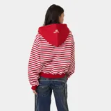 Campera con capucha de felpa de algodón, con diseño a rayas horizontales rojas y blancas, cierre frontal con cremallera bidireccional y bolsillos tipo canguro. Presenta grandes letras bordadas con el texto "EMESTUDIOS Madrid, 5135" en el pecho.