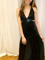 Vestido largo sin mangas con escote en V halter y aberturas laterales (cut-outs) en la cintura. El cuerpo superior presenta un llamativo diseño estampado multicolor, mientras que la falda larga es de tejido texturizado brillante en color verde esmeralda con inserciones godet en el ruedo.