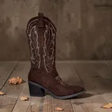 Bota texana de caña media en color café, confeccionada en material tipo gamuza. Presenta costuras decorativas en contraste y detalles de tachas metálicas en la caña. Cuenta con taco cuadrado y punta afilada.