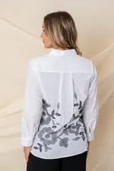 Camisa blanca de algodón con bordado floral en hilo negro en el frente. Camisa de corte clásico, con cuello abotonado, mangas largas con puños abotonados y cierre frontal con botones.