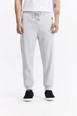 Pantalón de jogging color gris melange, confeccionado en tejido de algodón y poliéster. Presenta cintura elástica con cordón de ajuste, bolsillos laterales con cierre y puños elásticos en los tobillos.