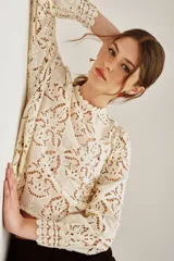Camisa de encaje color crema con diseño floral calado, cuello redondo con detalle de volado y mangas largas con puños ajustados.