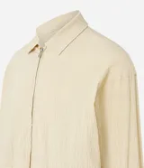 Campera color beige claro de algodón con textura arrugada, cuello inglés, cierre con cremallera, bolsillos laterales, elástico en la cintura y puños.