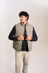 Chaleco puffer de corte regular, color beige, con cierre frontal y cuello alto. Presenta un diseño acolchado horizontal y logo bordado en el pecho.