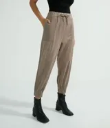 Pantalón estilo jogger confeccionado en suedine, con cintura elástica y cordón ajustable. Presenta recortes frontales, bolsillos laterales y detalles perforados decorativos en los laterales y bolsillos. El diseño incluye puños elásticos en la parte inferior.