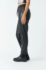 Pantalón negro de cuero sintético, tiro medio, con cintura ajustable, bolsillos laterales y corte holgado.