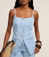 Chaleco largo de jean con escote recto, breteles finos ajustables y cierre frontal con botones. Presenta un corte acinturado con pences, bolsillos delanteros decorativos y ruedo en punta.