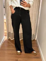 Pantalón de jean negro de corte recto y relajado, con costuras a contratono en color blanco. Presenta cintura con botón y cierre, bolsillos laterales y ruedo desflecado.