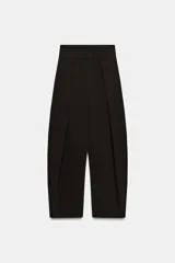 Pantalón de tiro alto con diseño tipo balloon, confeccionado en tejido con viscosa. Presenta pliegues frontales, bolsillos laterales ocultos en costura y cierre frontal con cremallera, botón interior y ganchos metálicos.