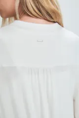 Bata de estar por casa color blanco, confeccionada en tejido suave con caída fluida. Presenta mangas tres cuartos con detalles de transparencias en los puños y el ruedo, bolsillos laterales y un lazo ajustable en la cintura.