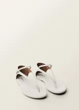 Sandalias planas de cuero color blanco, con tira delantera y tira al tobillo con hebilla.