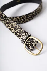 Cinturón de cuero con textura de pelo y estampado animal print de leopardo. Cuenta con una hebilla metálica de tono bronce envejecido y dos pasadores a juego.