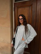 Conjunto de dos piezas color gris melange, confeccionado en tela de lanilla, compuesto por un buzo de manga larga con diseño cruzado al frente y un pantalón largo de corte holgado y tiro alto.