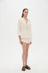 Blusa de algodón blanco con diseño de broderie, cuello en V y cierre con lazos frontales, mangas largas de corte holgado.