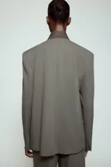 Blazer de corte estructurado en color verde oliva, con cuello subido en tejido a contraste de textura aterciopelada. Presenta cierre frontal con un solo botón, bolsillos con solapa en el delantero y un bolsillo superior tipo ojal.