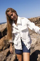 Chaqueta de denim liviana color blanco con volados en el frente, cuello camisero y cierre frontal de botones. Presenta un calce relajado y bolsillos funcionales.