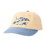 Gorra Rip Curl modelo Aots Ty Williams, de diseño bicolor con cuerpo en tono beige y visera curva en color celeste. Cuenta con un bordado frontal detallado que ilustra a personas cargando tablas de surf junto al logotipo de la marca.