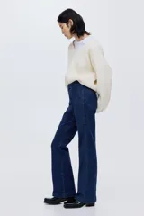 Jean de tiro alto con corte acampanado desde la rodilla. Presenta pliegues frontales y traseros, cierre con botón oculto y bolsillos traseros decorativos.