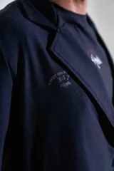 Blazer de lycra color negro, de corte oversize y diseño estructurado con solapas clásicas. Presenta detalles bordados sutiles en la solapa y en el puño de la manga.