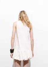 Vestido corto de algodón con diseño recto y sin mangas. Presenta cuello redondo y un bajo abullonado con detalle de volado. Incluye cierre de botón en la parte posterior y forro interior.