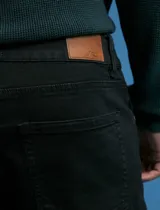 Pantalon denim de cinco bolsillos, corte recto y color negro, con botones y remaches metálicos en tono plata viejo.