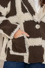 Chaqueta oversize con diseño de cuadros en relieve, confeccionada en una combinación de lana y poliéster con textura tipo borreguillo. Presenta un corte holgado, cuello con solapas y un botón joya central.