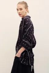 Camisa de seda negra con estampado geométrico de líneas verticales con rombos pequeños en tonos claros, cuello camisero, mangas largas con tajitos en los puños y cierre frontal con botones.