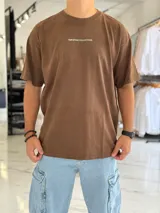Remera oversize de manga corta color marrón con efecto gastado. Presenta inscripciones estampadas en color blanco en el frente y en la espalda.