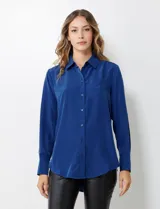 Camisa de satén color violeta, con cuello clásico, cierre frontal con botones, manga larga con puños anchos abotonados y bolsillo aplicado en el pecho.
