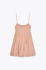 Vestido corto color rosado pálido, con escote recto fruncido con elástico y detalle de encaje en el borde superior. Posee tirantes finos ajustables y falda escalonada con volados.