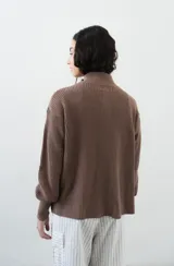 Saco tejido de punto color amarillo claro, con cuello alto asimétrico abotonado, botones oscuros contrastantes en la parte frontal y mangas largas con puños ajustados.