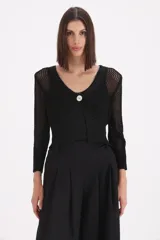 Saco corto de tejido de punto con acabado en lurex, de manga larga y escote en V con cierre de un solo botón frontal. Presenta una textura calada en las mangas y el cuerpo.