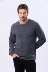 Remera de algodón texturada color gris oscuro, de manga larga, con cuello redondo y botones en la parte frontal. Presenta un pequeño logo bordado en el pecho y un parche decorativo en la manga izquierda.