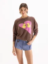 Buzo marrón de cuello redondo, mangas largas y calce amplio con efecto lavado desgastado. Presenta un diseño estampado en el frente con un corazón rosado y dos patitos.