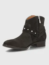 Bota corta de mujer color gris oscuro o marrón oscuro, estilo botín biker, confeccionada en gamuza. Presenta una tira decorativa con tachas metálicas plateadas y hebilla. Tiene un taco bajo y punta ligeramente afilada.
